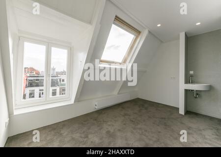Empty mansard room with light walls with windows and mounted lights in ceiling Stock Photo
