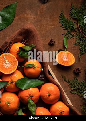Top view heap of fresh orange mandarin with leaves placed in container with textile on table with green twigs in room Stock Photo