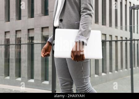 Crop anonymous African American businessWoman in formal clothes standing near glass fence with laptop Stock Photo
