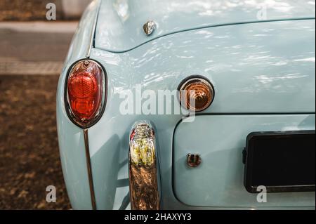 Part of blue bumper of old timer automobile with headlight and vintage design parked on pathway near pavement on street of city Stock Photo