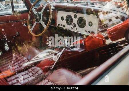 Through window with reflections of old fashioned automobile with steering wheel and dashboard with leather seats parked on street of city Stock Photo