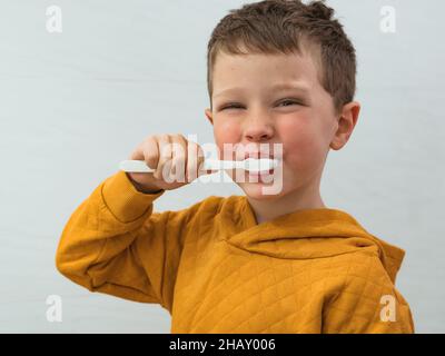 Cute smiling boy in casual wear brushing teeth in bathroom during morning hygienic routine at home looking at camera Stock Photo