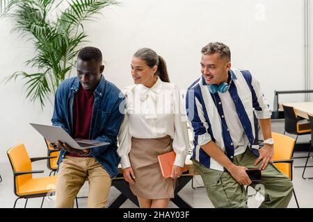 Group of positive multiracial coworkers surfing on netbook while working on business project together at table in light modern office Stock Photo