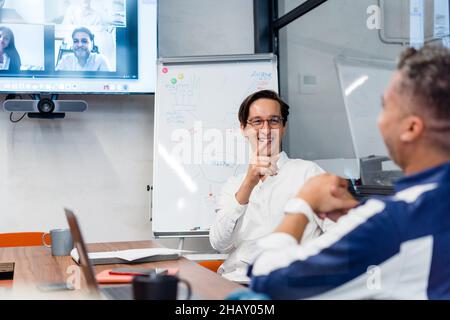 Coworkers sitting at table with gadgets and documents in modern workspace with white flip chat during online conference in office Stock Photo