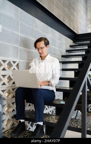 Focused male worker with netbook sitting on staircase while working in light modern workspace during work Stock Photo