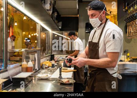 Side view of male cook in protective mask and apron using gas burner while preparing o fry bone marrow during work in cafe Stock Photo
