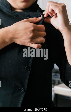 Crop anonymous female buttoning up black jacket of chef uniform while working in modern restaurant Stock Photo