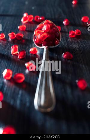 Red fresh juicy pomegranate fruits seeds on spoon and dark wooden surface on blue background Stock Photo