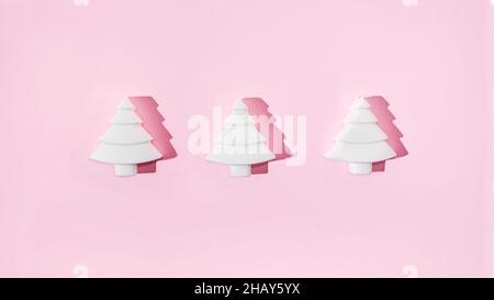 Three geometrical white Christmas trees on pastel pink background. Minimal romantic composition for Christmas or New Year's eve celebration or web ban Stock Photo