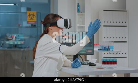 Lab worker using vr goggles with 3d projection in science laboratory. Woman scientist working with virtual reality headset to develop biochemistry simulation for analysis. Futuristic innovation Stock Photo