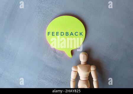 Feedback and review concept. Speech bubble with text FEEDBACK and wooden human figure on concrete floor. Copy space for text Stock Photo