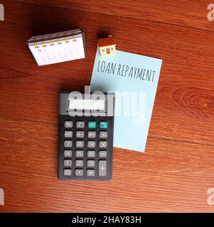 Planning and financial concept. Top view of desk calendar, calculator, miniature house and paper with text LOAN REPAYMENT Stock Photo