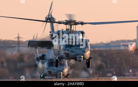 Two MH-60S Sea Hawks, assigned to Helicopter Sea Combat Squadron (HSC) 12, take off during a high altitude, low opening (HALO) parachute jump training at Yokota Air Base, Japan, Dec. 13, 2021. U.S. Marines and a U.S. Air Force Survival, Evasion, Resistance and Escape (SERE) specialist conducted week-long jump training using Air Force and Navy aircraft. The training supports the U.S. Indo-Pacific Command’s dynamic force employment (DFE) concept through agile combat employment (ACE), which supports the National Defense Strategy effort to conduct training with joint partners while maintaining glo Stock Photo