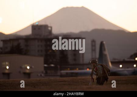 A Marine assigned to the 3rd Reconnaissance Battalion, 3rd Marine Division, recovers his parachute after conducting a high altitude, low opening (HALO) jump over Yokota Air Base, Japan, Dec. 13, 2021. U.S. Marines and an Air Force Survival, Evasion, Resistance and Escape (SERE) specialist conducted week-long jump training using Air Force and Navy aircraft. The training supports the U.S. Indo-Pacific Command’s dynamic force employment (DFE) concept through agile combat employment (ACE), which supports the National Defense Strategy effort to conduct training with joint partners while maintaining Stock Photo