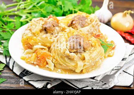 Twisted pasta with meatballs in the center with cream sauce, stewed tomatoes, bell peppers, onions and garlic in white plate on a napkin against dark Stock Photo