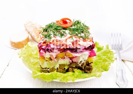 Puff salad with beef, boiled potatoes and beets, pears, spicy carrots, seasoned with mayonnaise and garnished with dill on a green lettuce in a plate, Stock Photo