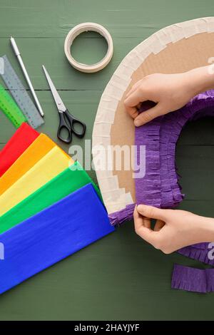 Woman making Mexican pinata with purple paper on green wooden background Stock Photo
