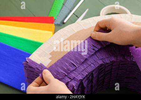 Woman making Mexican pinata with purple paper on green wooden background, closeup Stock Photo