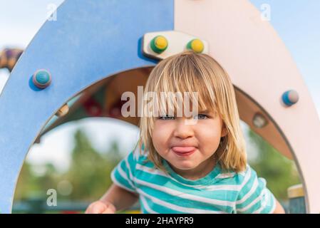naughty little boy sticking his tongue out in the playground Stock Photo