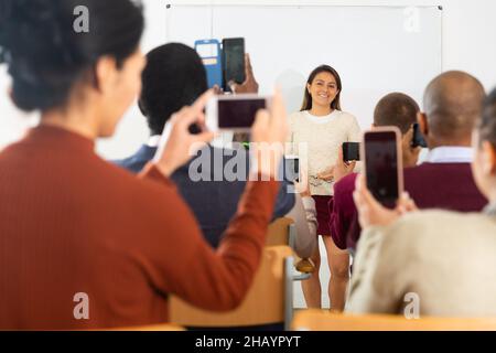Students shooting lesson on smartphones , teacher standing at blackboard Stock Photo