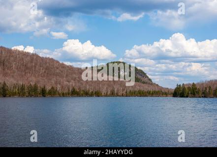 Spice Mountain - a granite cliff by Kettle Pond, in Groton State Park, VT. Mixed birch-spruce forest in spring. Cumulus clouds and ripple lake waters. Stock Photo