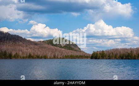 Spice Mountain - a granite cliff by Kettle Pond, in Groton State Park, VT. Mixed birch-spruce forest in spring. Cumulus clouds and ripple lake waters. Stock Photo