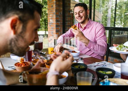 Young latin man eating mexican food tacos tostadas on a restaurant terrace in Mexico Latin America, feeling happy on a summer day