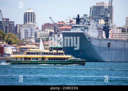 Sydney ferry the emerald class MV Catherine Hamlin travels past Garden Island navy base and HMAS Canberra on Sydney Harbour,NSW,Australia Stock Photo