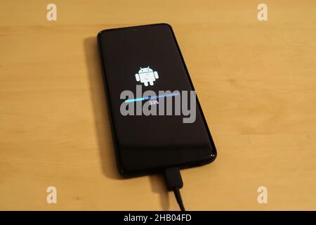 KIEL, GERMANY - Nov 13, 2021: A smartphone on a wooden surface with the progress indicator of an Android operating system update Stock Photo
