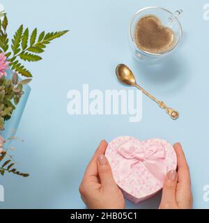 Woman's hands with a gift box and a cup of coffee on the blue background. Top view. Stock Photo