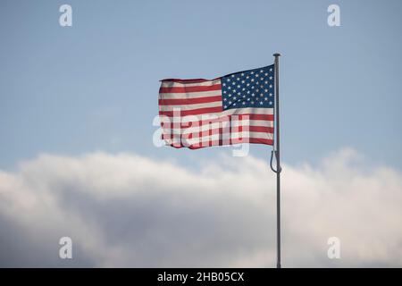 Stars and Stripes American flag on flagpole  against a blue sky with dark cloud approaching. Stock Photo