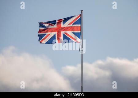 Union Jack British flag on flagpole  against a blue sky with dark cloud approaching. Stock Photo