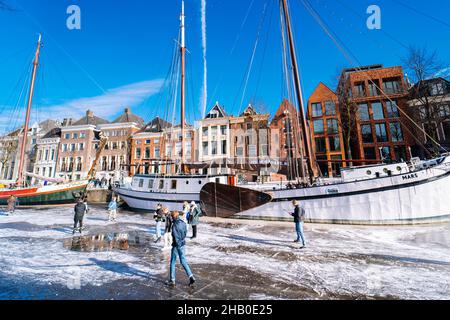 People ice scating on frozen canal in city center in Netherlands. Peoples making pictures, walking and skating on frozen canal in winter. Winter fun in cityGroningen. Netherlands. 14.02.2021 Stock Photo