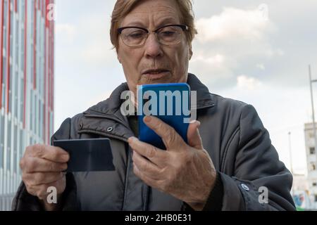Senior woman using a credit card with smartphone, outdoors. Stock Photo