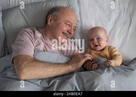cheerful senior grandfather resting with his grandson on bed at the morning having a nap Stock Photo