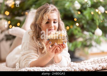Smiling blonde woman with golden christmas gift box near christmas tree. Stock Photo