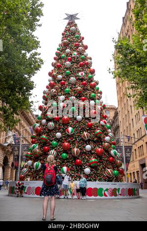 Sydney. 16th Dec, 2021. People take photos beside a Christmas tree in Sydney, Australia on Dec. 16, 2021. As Australians crowd into shopping centers to buy last-minute Christmas presents and prepare to gather with their families over the summer holidays, the nation is simultaneously facing a looming wave of the Omicron variant of COVID-19.TO GO WITH 'Roundup: Omicron wave looms over Aussie Christmas, experts urge caution on health measures' Credit: Bai Xuefei/Xinhua/Alamy Live News