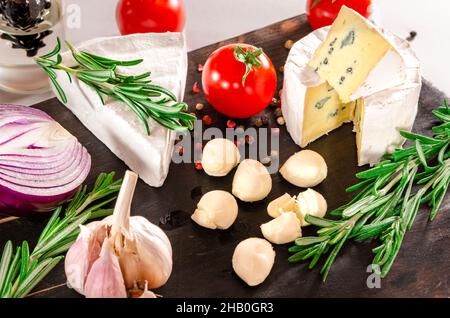 Tomatoes with mozzarella , basil and rosemary. Assorted cheeses on wooden board. Stock Photo