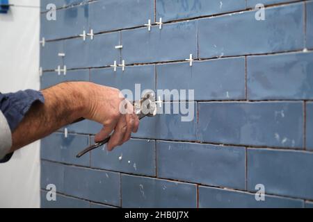 Constructor worker hand removing the separation between tiles on the wall. Stock Photo