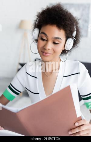 happy african american woman in wireless headphones looking at folder Stock Photo