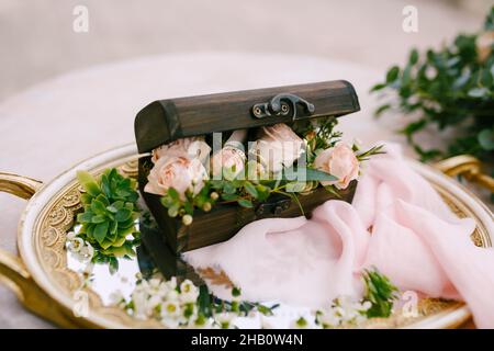 Wooden box with rings and tea roses stands on a plate at the reception table Stock Photo