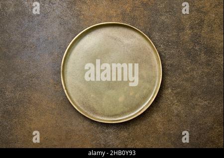 Empty green rustic ceramic plate with black rim on brown rustic background, flat lay, copy space Stock Photo