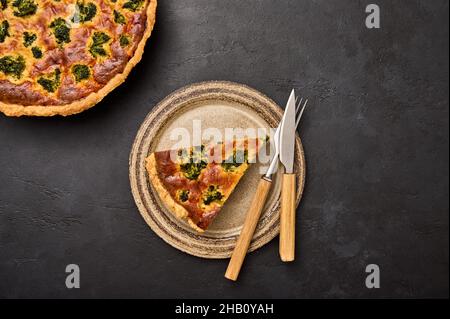 Piece of quiche tart on ceramic rustic plate with knife and fork on black graphite background. Top view Stock Photo