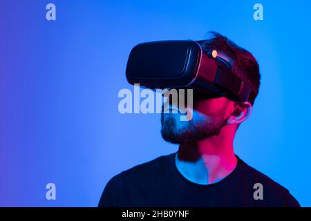 Portrait of man using VR headset while playing a video game in dark interior illuminated neon light. Close-up futuristic googles with colored light. Stock Photo