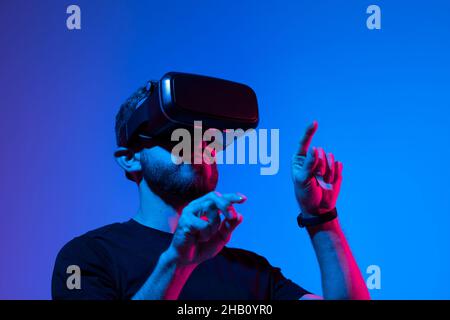 Happy and excited man playing racing video game with virtual reality headset in a metaverse world with a friends. Future technology concept. Stock Photo