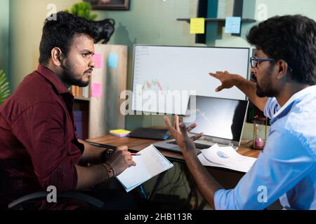 Traders analysing by discussing about stock market charts while working at office - concept of teamwork, learning or planning share market strategy Stock Photo