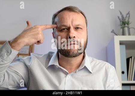 Middle aged man pointing  forefinger on his temple. Office worker. Confused man in trouble. Stock Photo