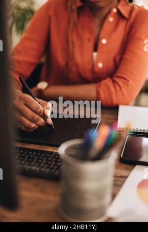 Graphic designer drawing on a digital tablet. Unrecognizable young woman sitting in front of a computer at her desk. Creative female freelancer workin Stock Photo