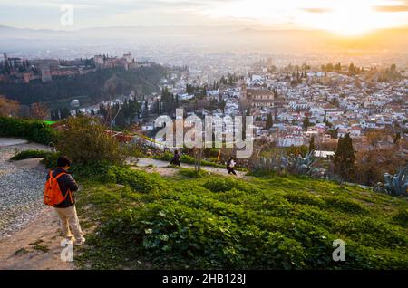 Granada, Andalusia, Spain - January 17th, 2020 : A tourist looks at the Alhambra palace and Unesco listed Albaicin district  at sunset.