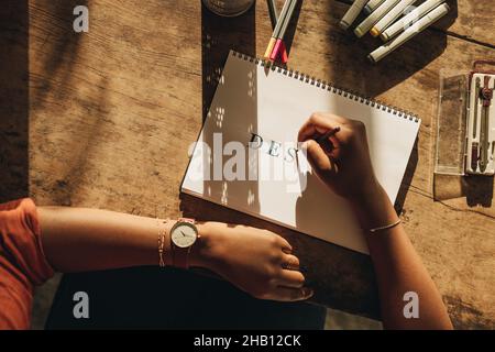 Female freelancer drawing the word ''DESIGN'' while sitting at her workstation. High angle view of a female graphic designer working on a new project.
